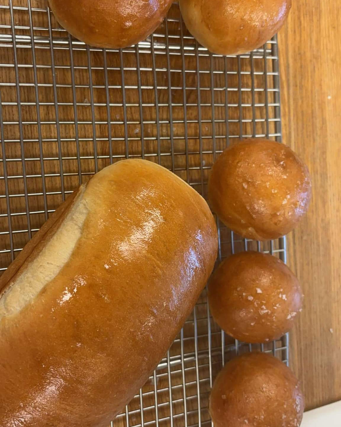Glossy brioche loaves and dinner rolls on a wire cooling rack